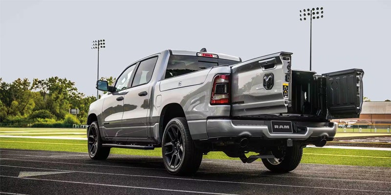 Rear view of a silver Ram pickup truck with its multi-functional tailgate open, on a track field.