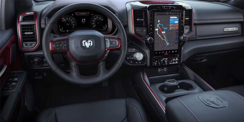 Interior of a car with black and red trim, including a steering wheel, dashboard, and large touchscreen displaying a map.