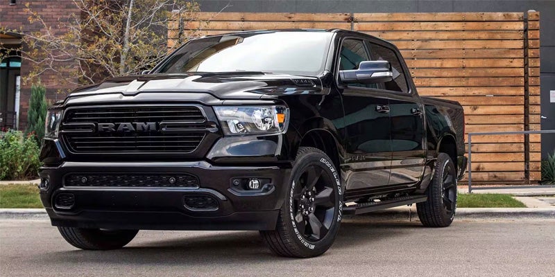 A sleek, all-black Dodge Ram pickup truck parked on asphalt with a wooden fence and building in the background.