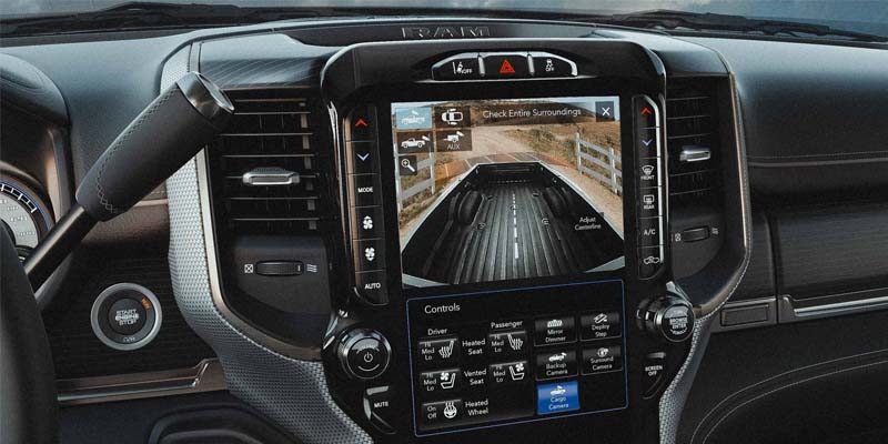 Inside a RAM truck, dashboard infotainment screen shows a clear rear-facing bed camera view, with various controls.