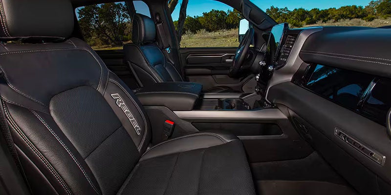Front interior view of a truck, showing black leather seats with Rebel embroidered on the driver's side.